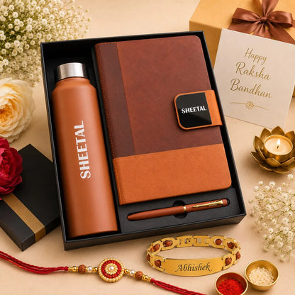 A Raksha Bandhan gift set in a black box, featuring a terracotta-colored SHEETAL insulated bottle, a brown and orange leather notebook with a matching pen, a gold Abhishek bracelet, and festive decorative elements on a beige background.