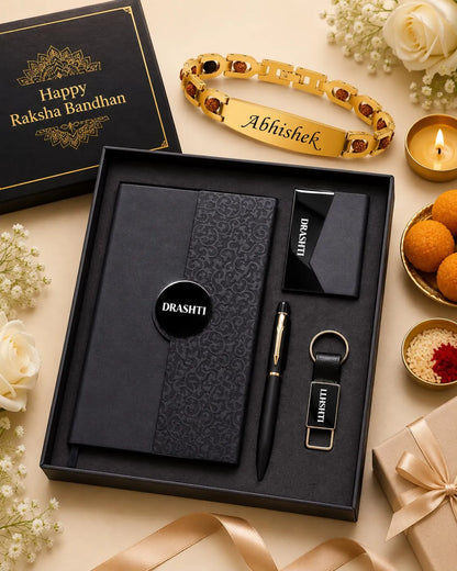 A personalized Raksha Bandhan gift set displayed in an open black box on a beige surface. The set includes a black notebook with a subtle damask pattern, a black pen, a black keychain with a nameplate, a black card holder, and a black circular logo sticker.