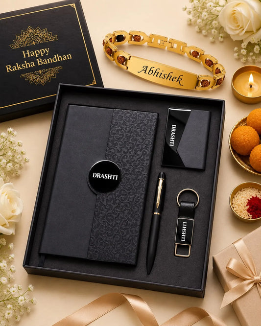 A personalized Raksha Bandhan gift set displayed in an open black box on a beige surface. The set includes a black notebook with a subtle damask pattern, a black pen, a black keychain with a nameplate, a black card holder, and a black circular logo sticker.