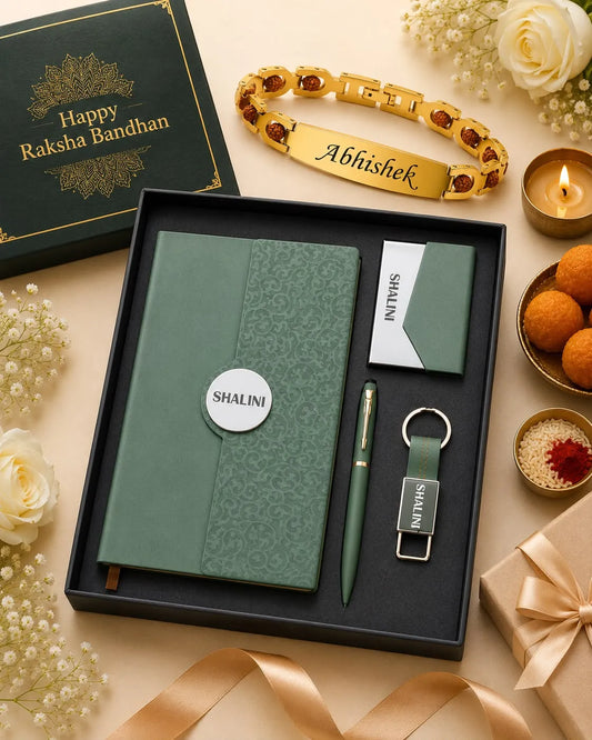 A personalized Raksha Bandhan gift set in a black box, featuring a green patterned notebook, matching pen, keychain, and card, alongside a gold engraved bracelet. The set is styled on a beige surface with decorative flowers, a lit candle, and a green gift box.