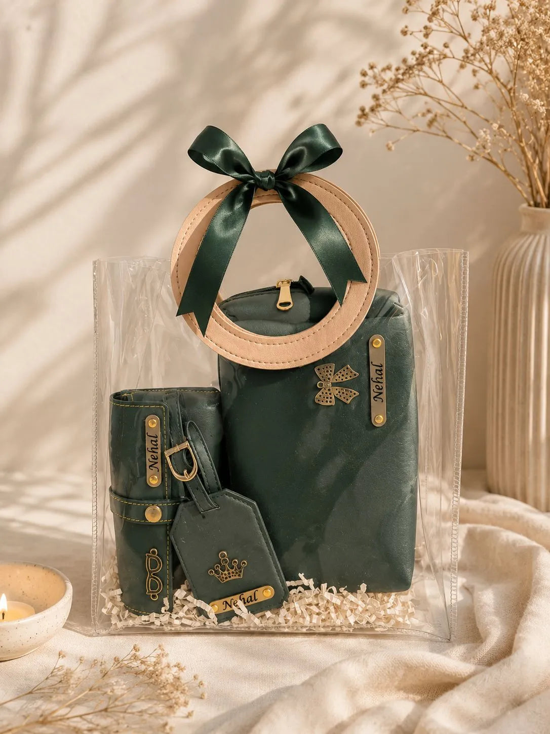 A coordinated dark green leather accessory set arranged inside a clear plastic gift bag with a wooden handle and green ribbon. The set includes a small pouch, a larger bag, a matching wallet or card holder, and a luggage tag, all with gold-tone hardware and decorative emblems.