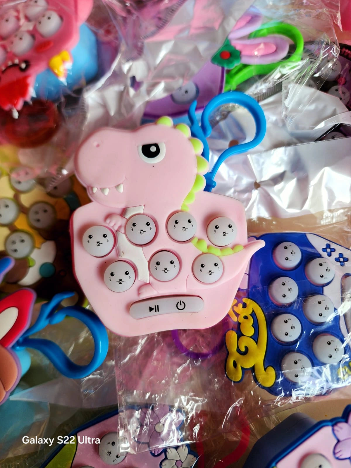 Pink toy phone with cartoon face buttons surrounded by colorful toys on a reflective surface.