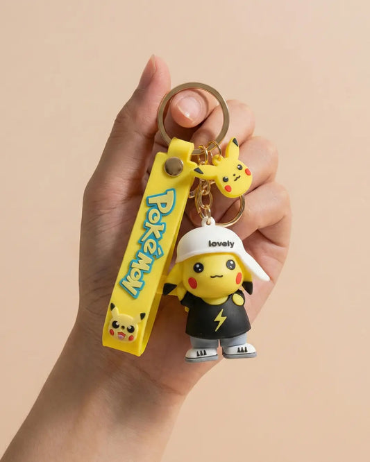 Hand holding a keychain with Pikachu figures and a Poké Ball-shaped clip on a beige background