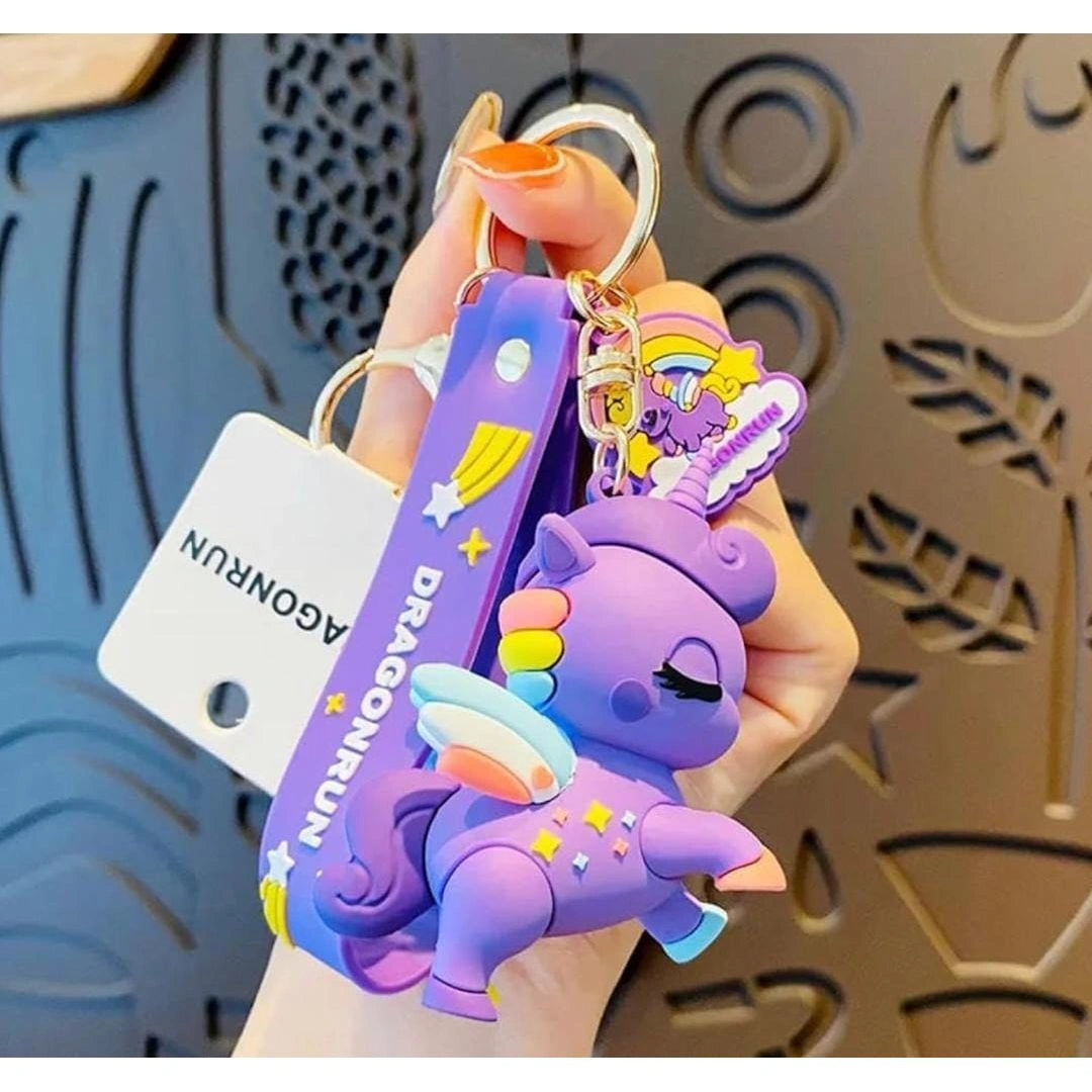 Purple unicorn keychain with a lanyard held by a hand against a decorative background.