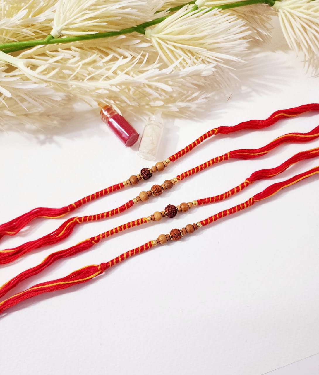 Red and gold beaded bracelets on a white background with dried plants.