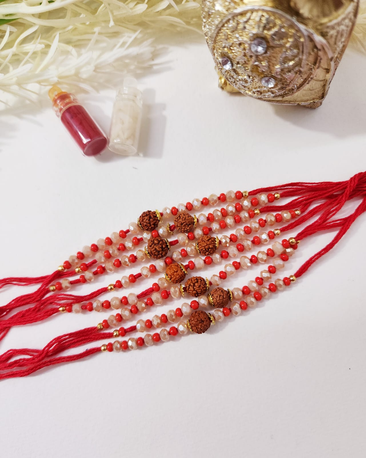A set of red colored rakhi with Rudraksh beads and decorative elements, displayed alongside a decorative golden object.