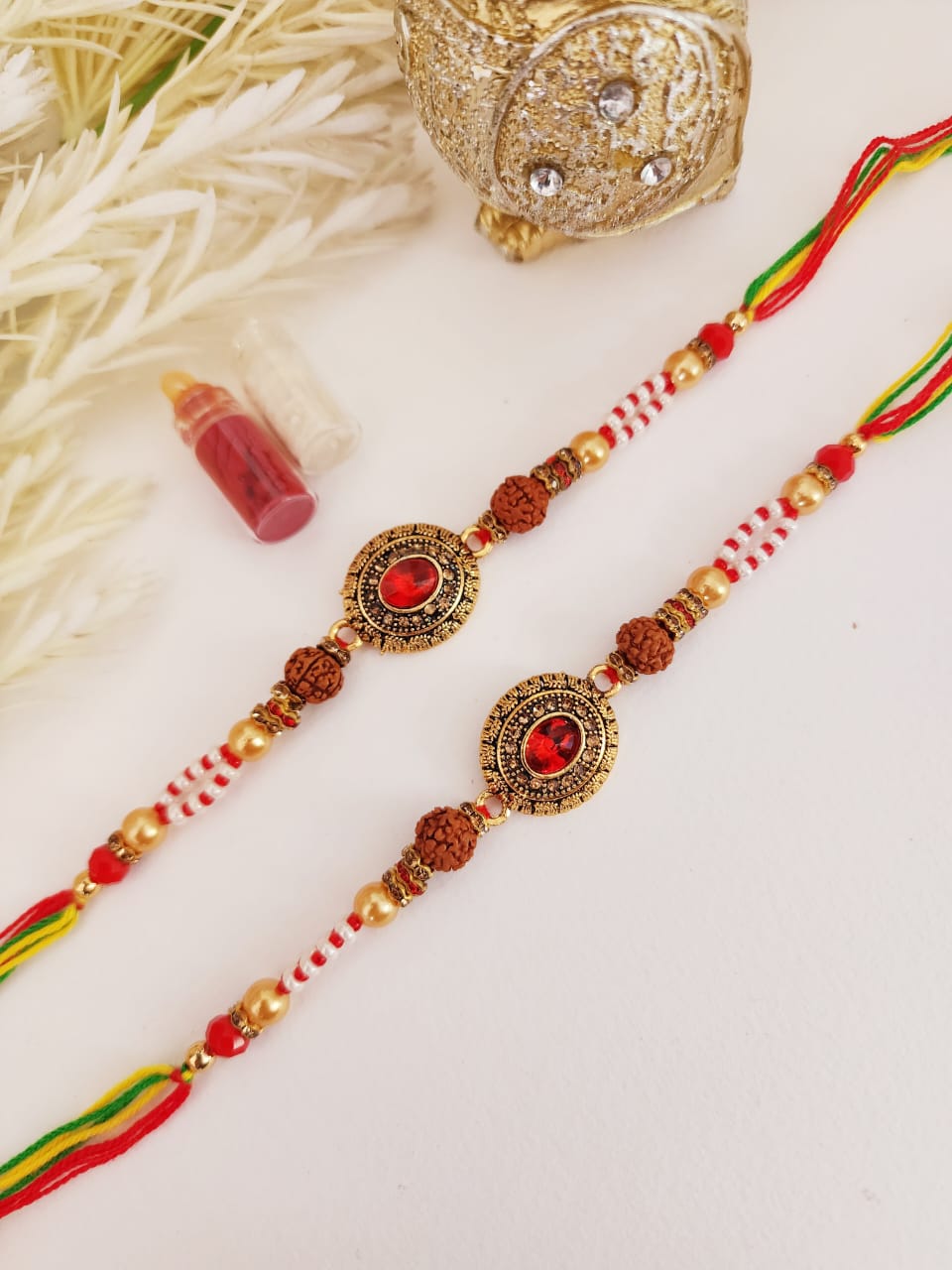 Two Rudraksh Rakhi bracelets with red and gold colors, displaying authentic Rudraksh beads, placed on a white surface.