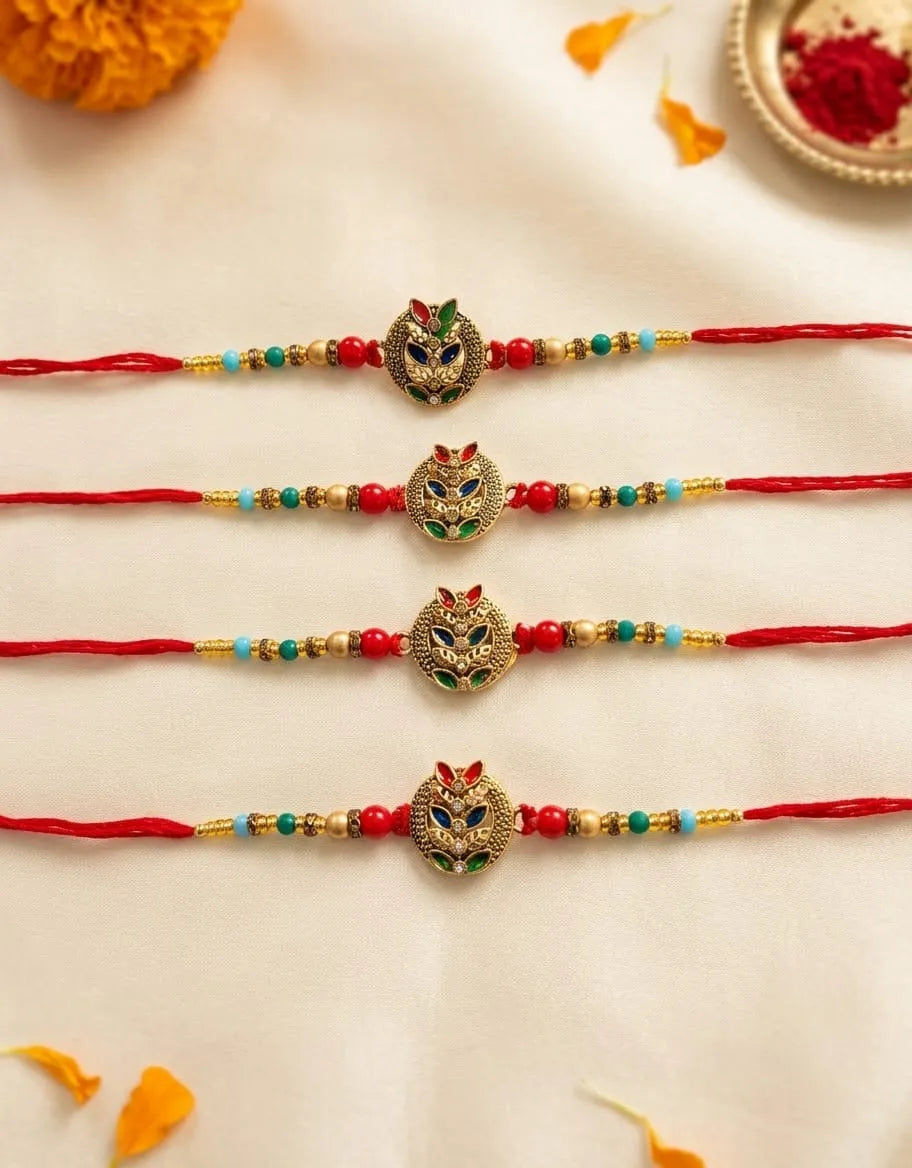 Four red string rakhi bracelets with gold-tone owl pendants and colorful bead accents, arranged vertically on a cream fabric background with decorative orange and red floral elements.