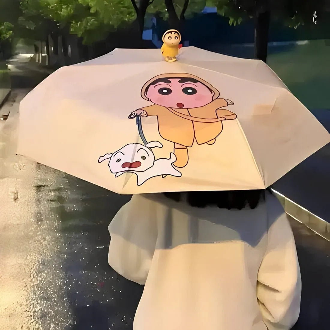 Person holding a cartoon-themed umbrella with a character and dog illustration on a rainy street.