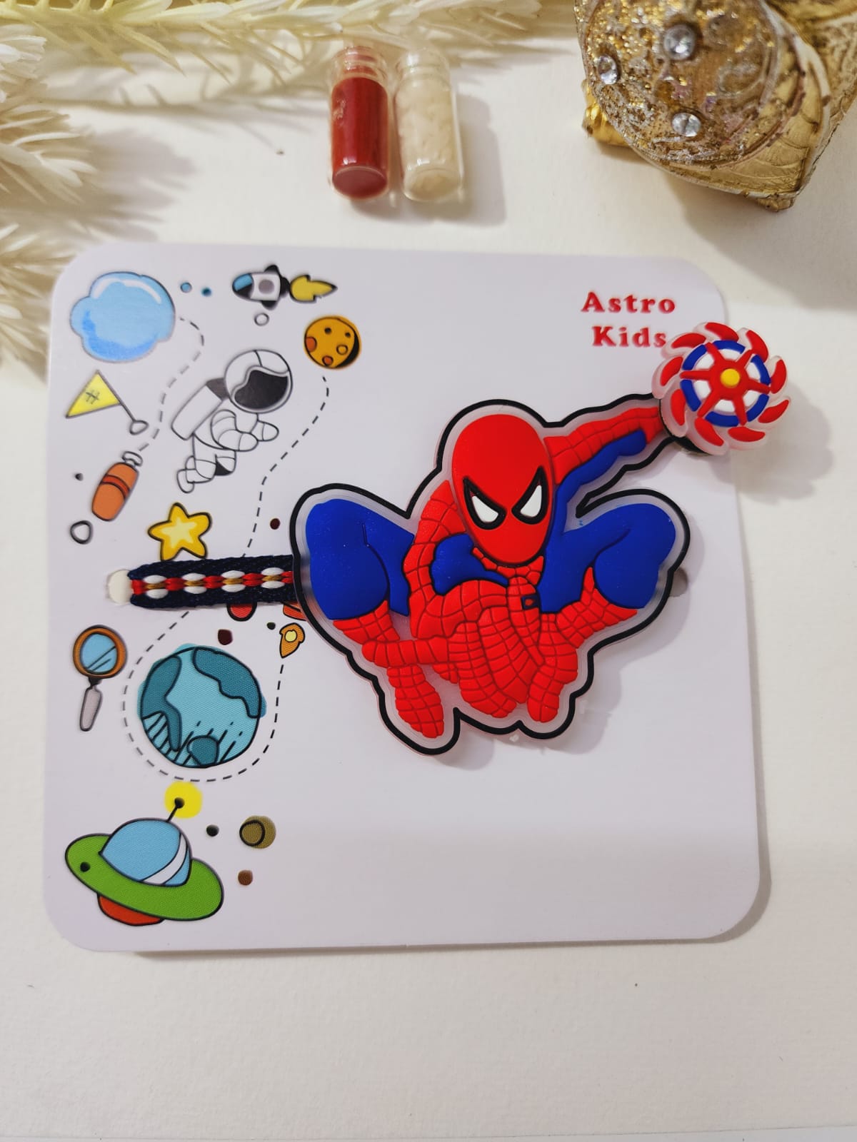 A colorful spinner rakhi featuring a cartoon character with a red and blue costume, surrounded by decorative elements like stars, planets, and a candy.
