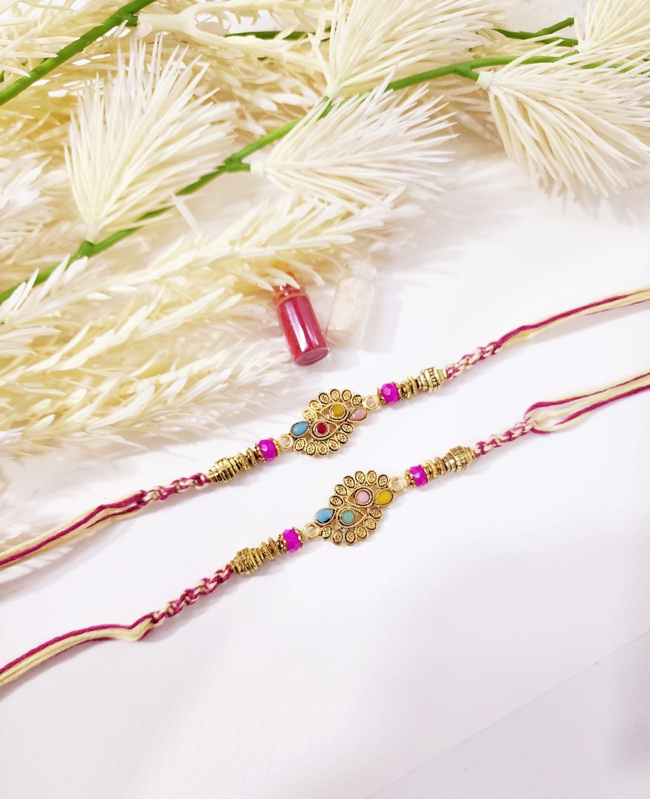 Two intricately designed rakhi (holy thread) on a white background with flowers.