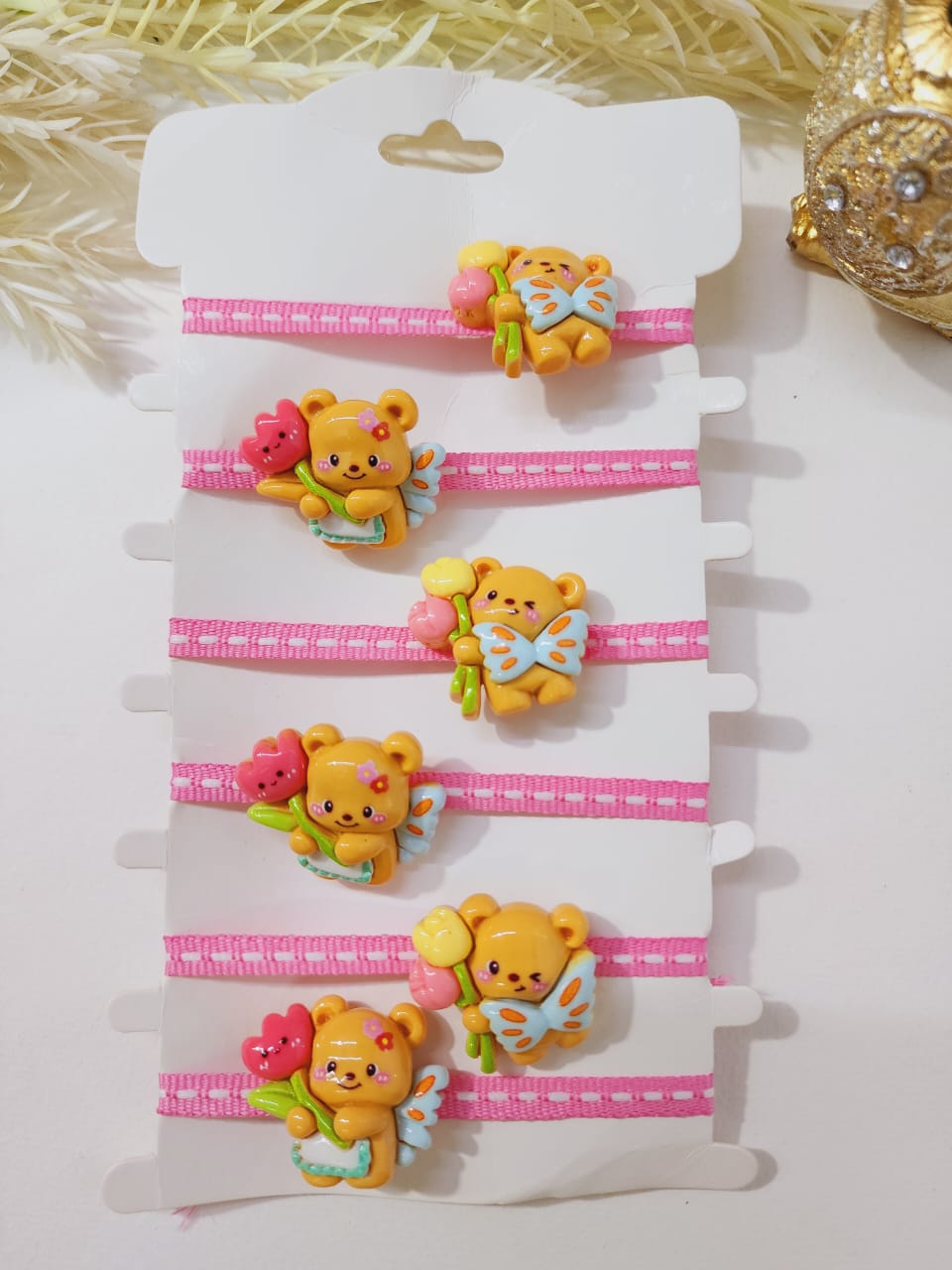 A set of colorful rakhis featuring a teddy bear and panda design, displayed on a white card with pink borders.