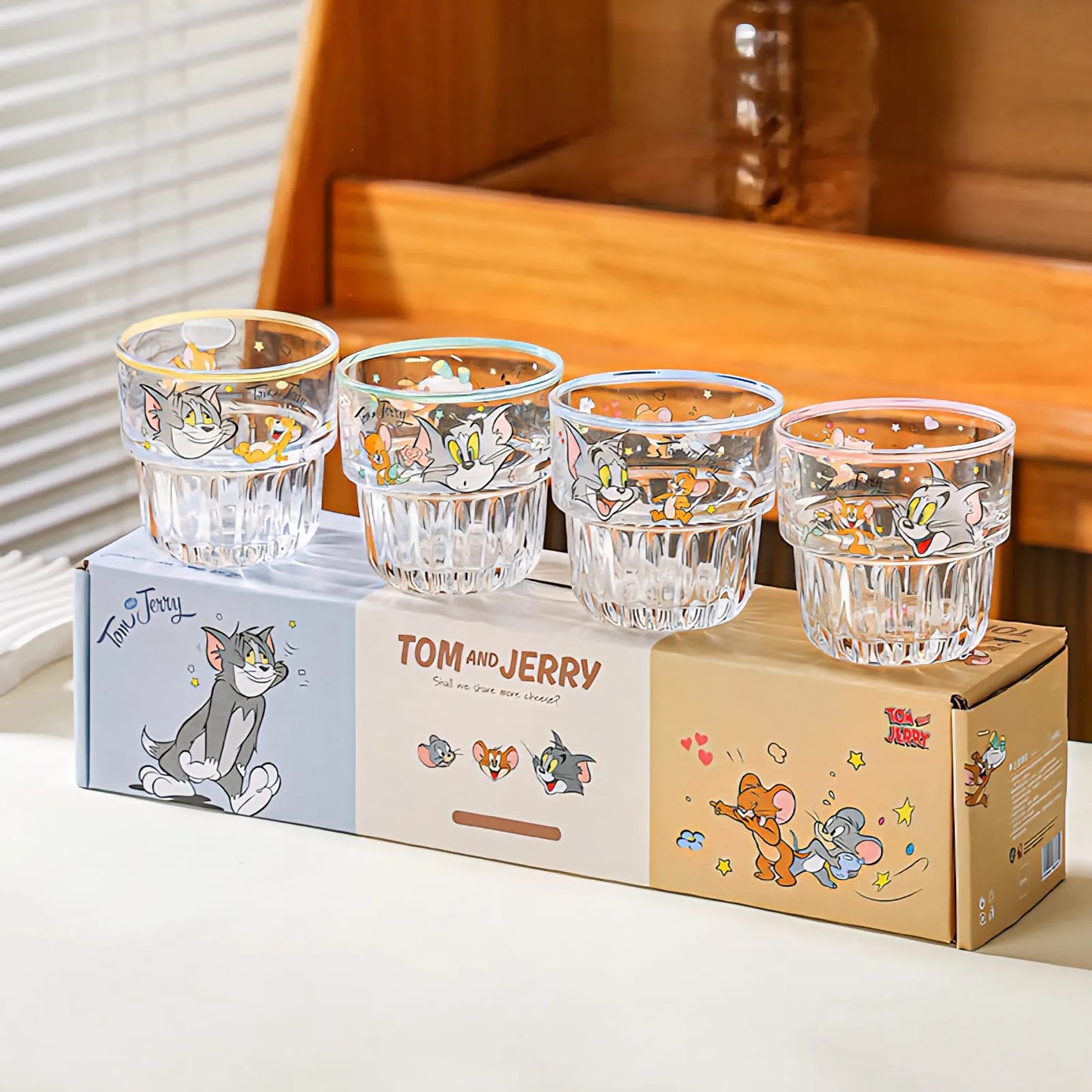 Four clear Tom and Jerry cartoon drinking glasses displayed on top of their illustrated retail box. The glasses have colorful printed character graphics, and the box is split into blue, cream, and tan sections with Tom and Jerry artwork and the text 'TOM AND JERRY'.