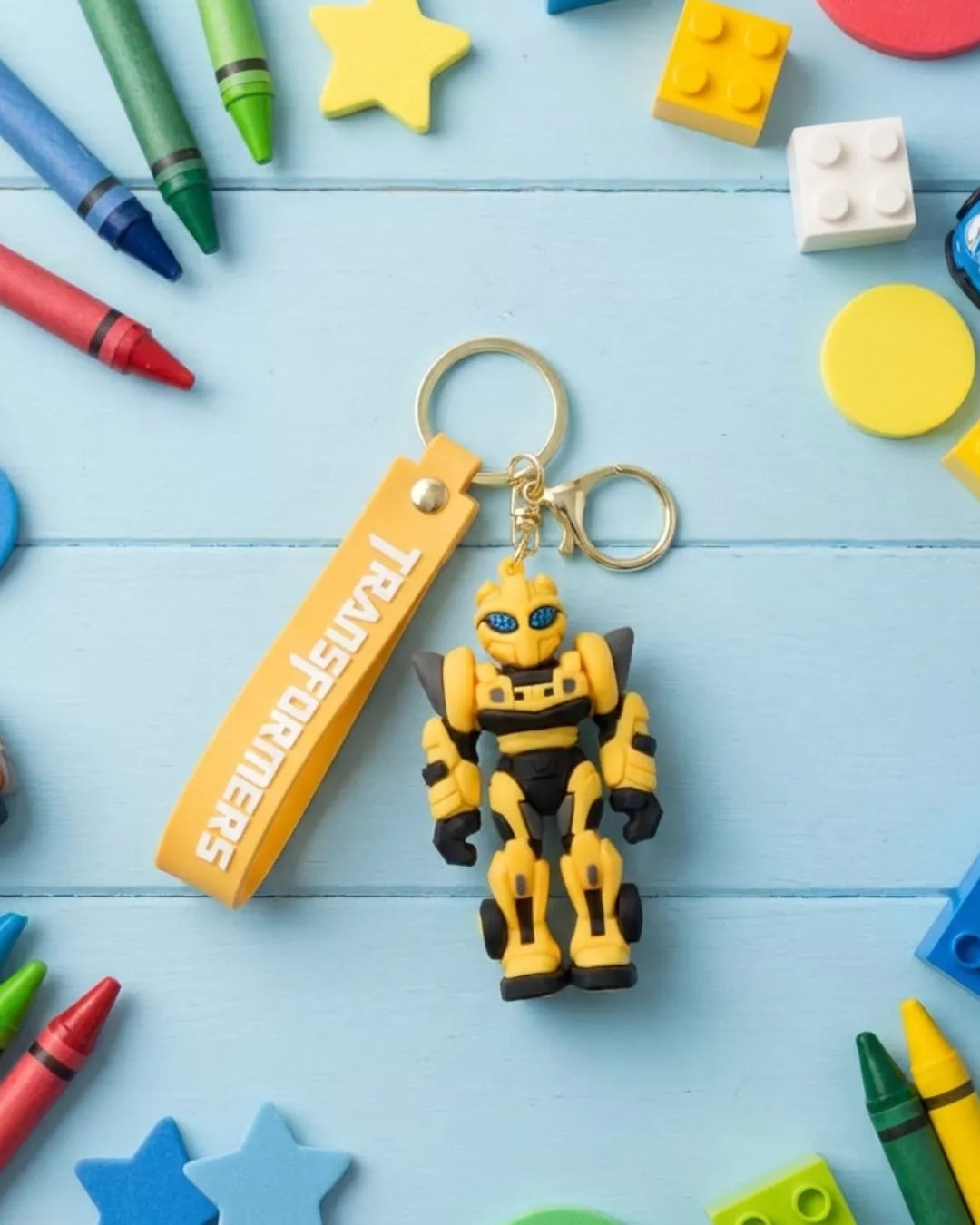 Toy robot keychain with 'Transformers' branding on a colorful wooden surface with toys and crayons.