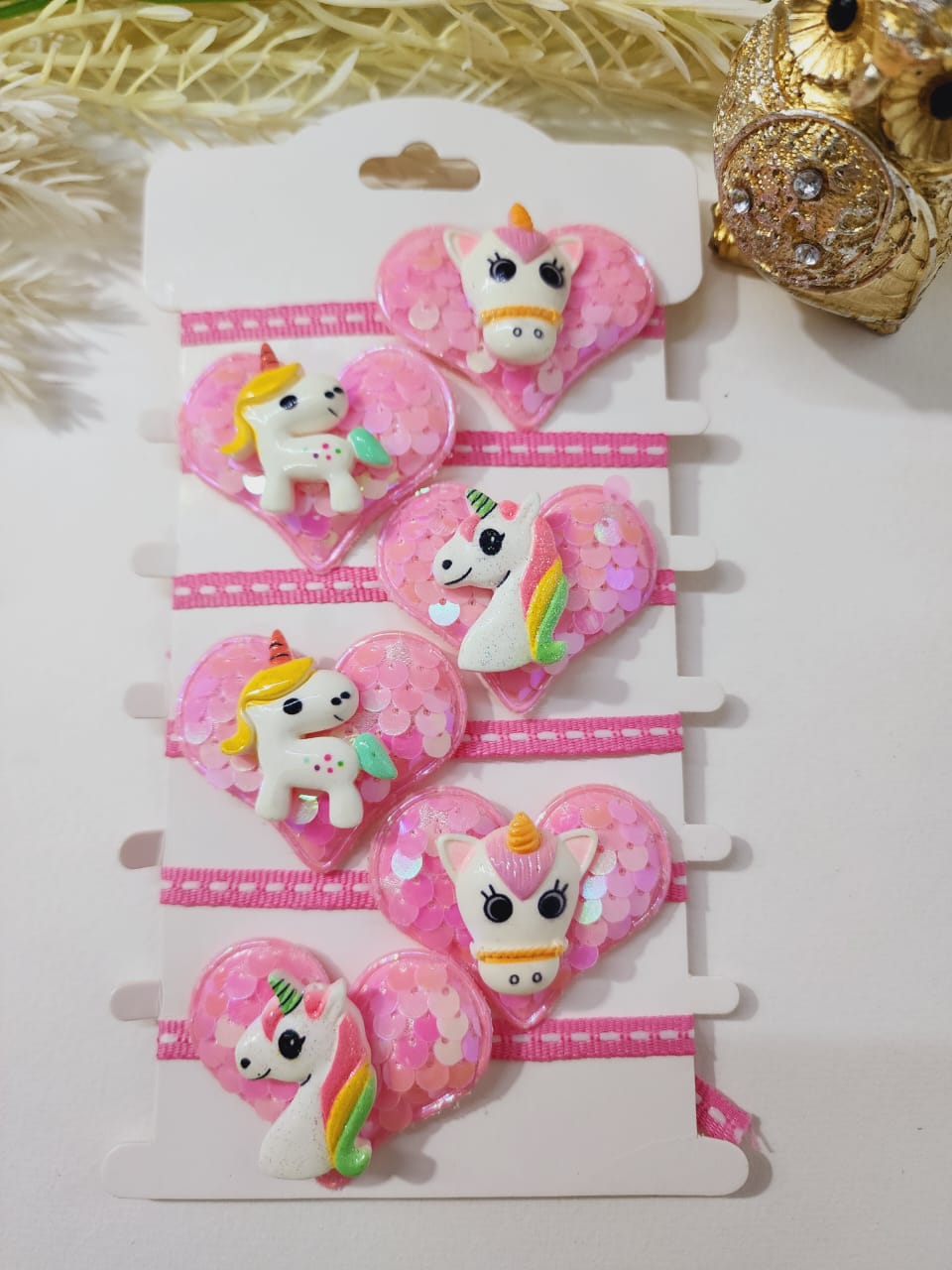 A collection of pink and white glittery rakhi bracelets with unicorn designs displayed on a card.