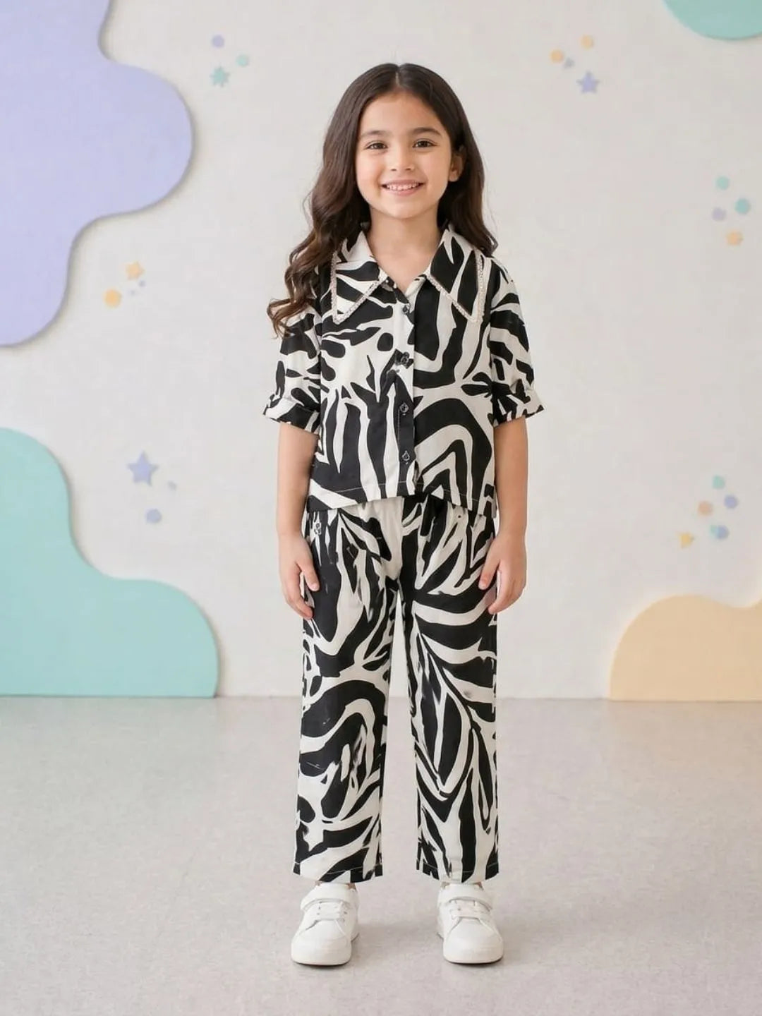 Young girl wearing a black and white patterned outfit standing against a colorful abstract wall.