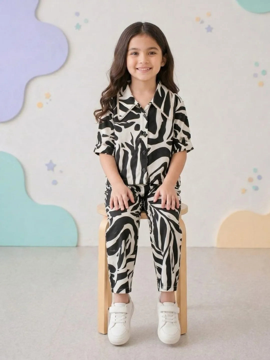 Child wearing a zebra print outfit sitting on a chair with a colorful wall background