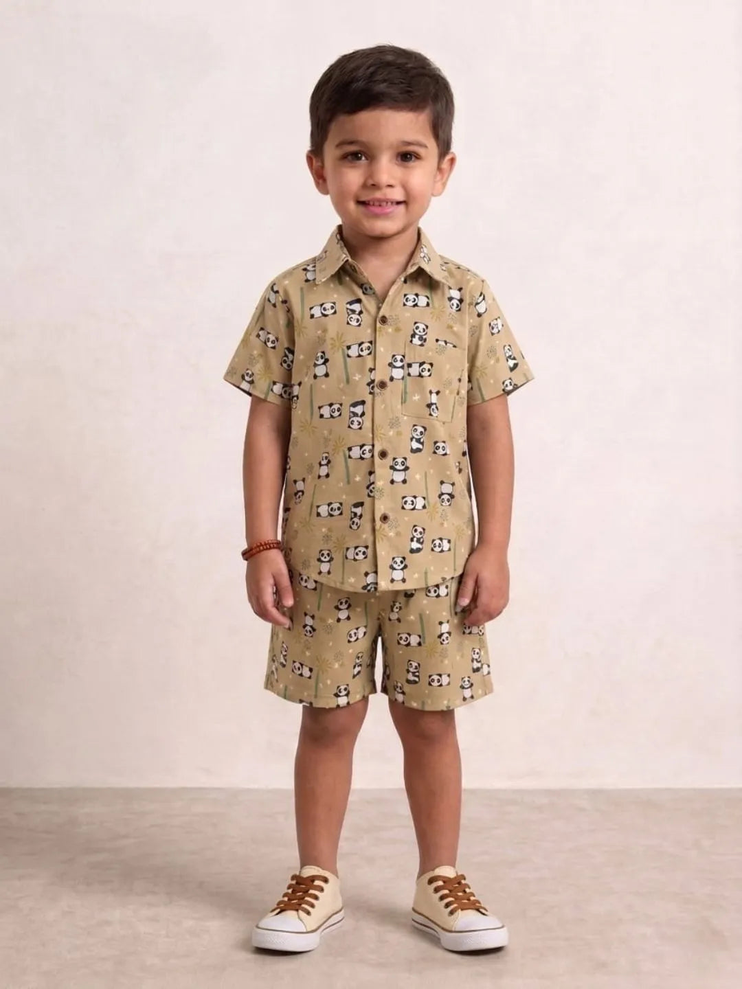 Child wearing a beige patterned shirt and shorts set with brown shoes on a plain background