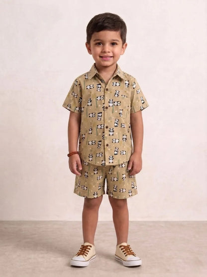 Child wearing a beige patterned shirt and shorts set with brown shoes on a plain background