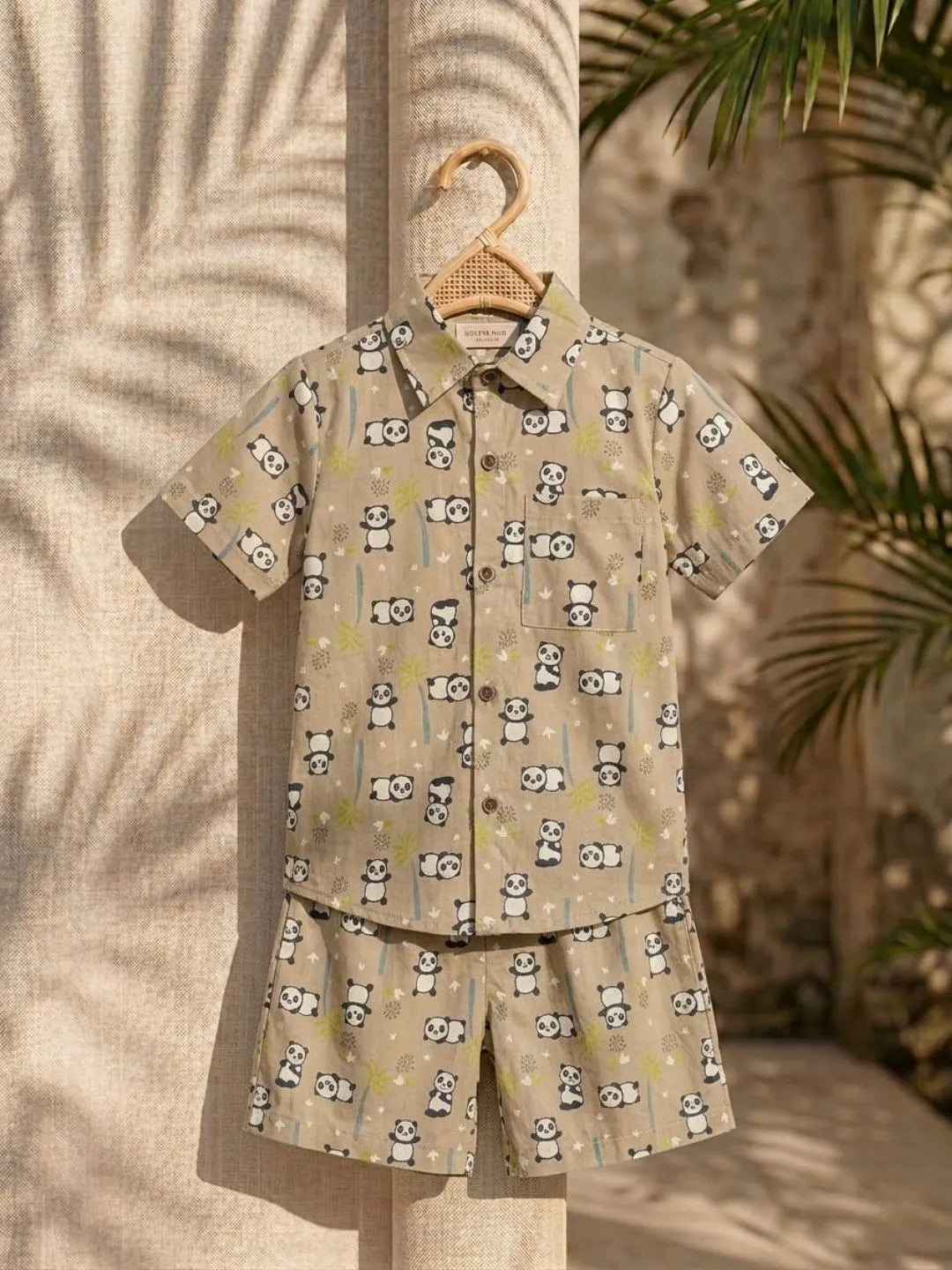 Children's shirt and shorts set with panda pattern on a hanger against a textured wall.