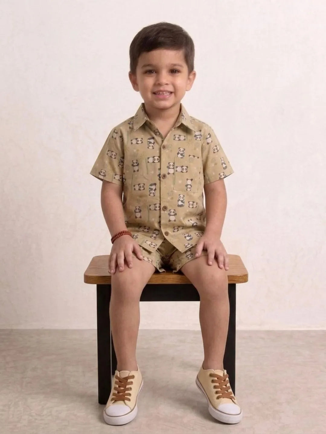 Child wearing a patterned shirt and shorts sitting on a wooden stool against a plain background