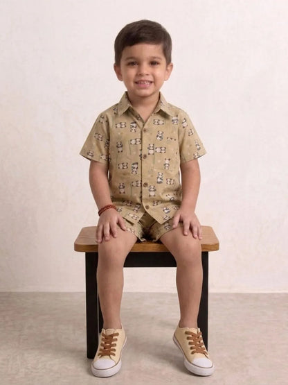 Child wearing a patterned shirt and shorts sitting on a wooden stool against a plain background