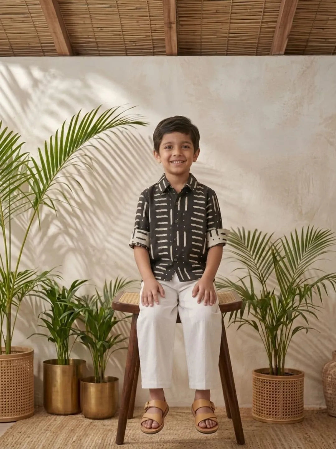 Boys black printed cotton shirt with white trouser co-ord set sitting pose summer outfit
