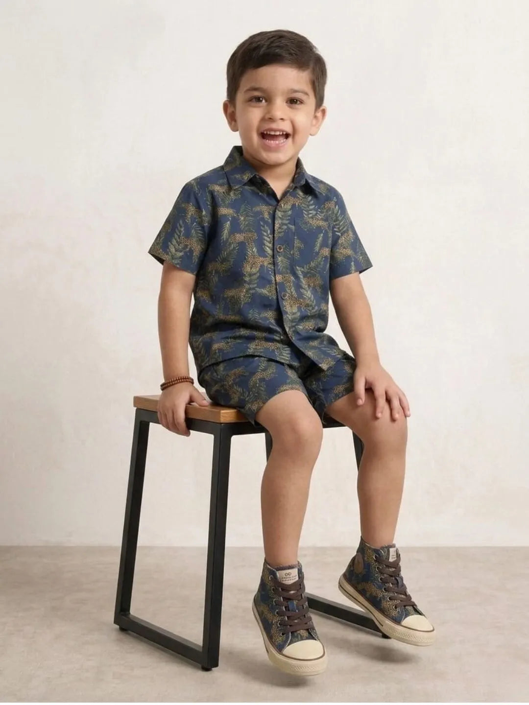 Child wearing a blue camouflage outfit sitting on a stool against a plain background