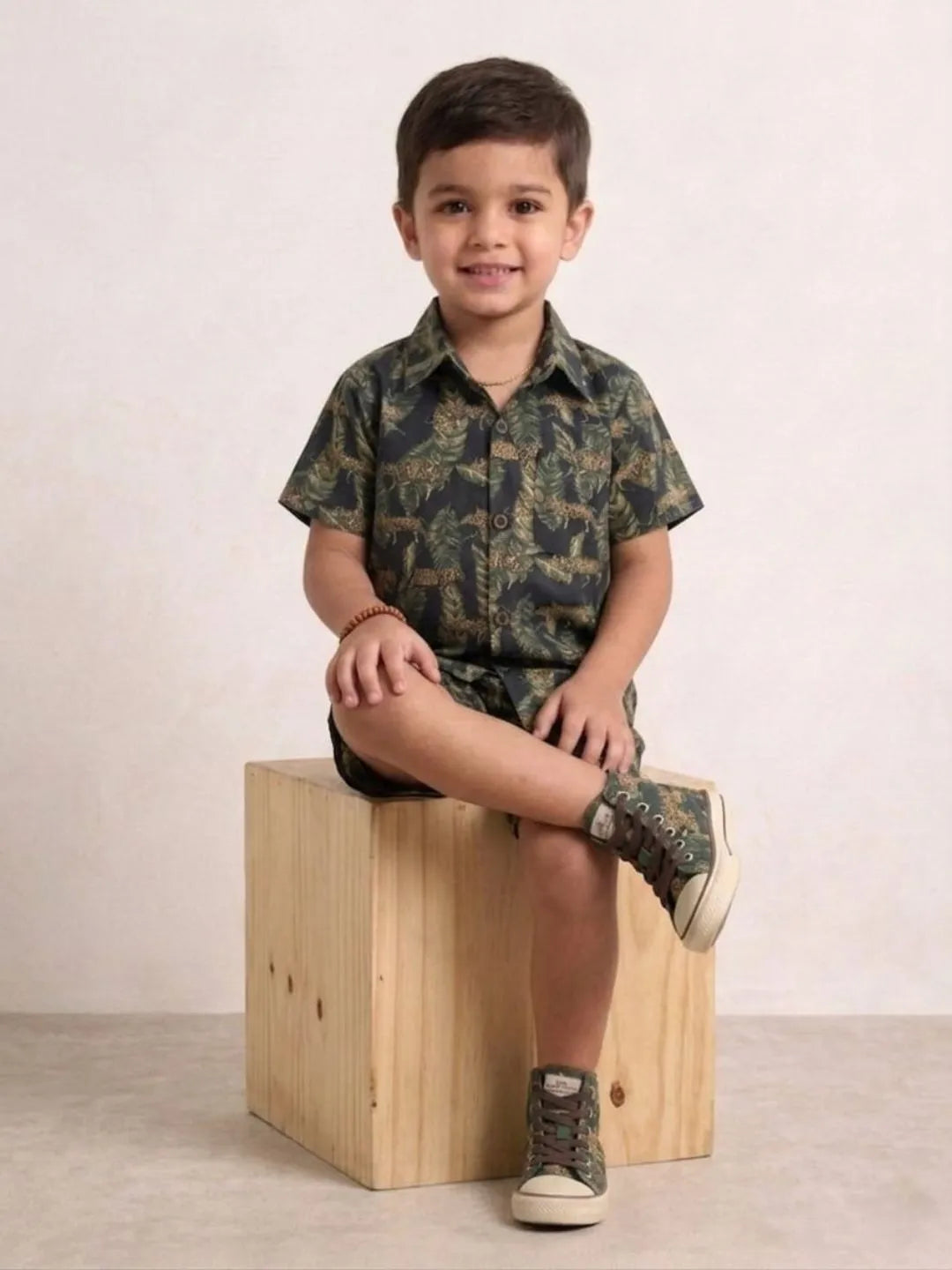 Child wearing a camouflage outfit sitting on a wooden block against a plain background