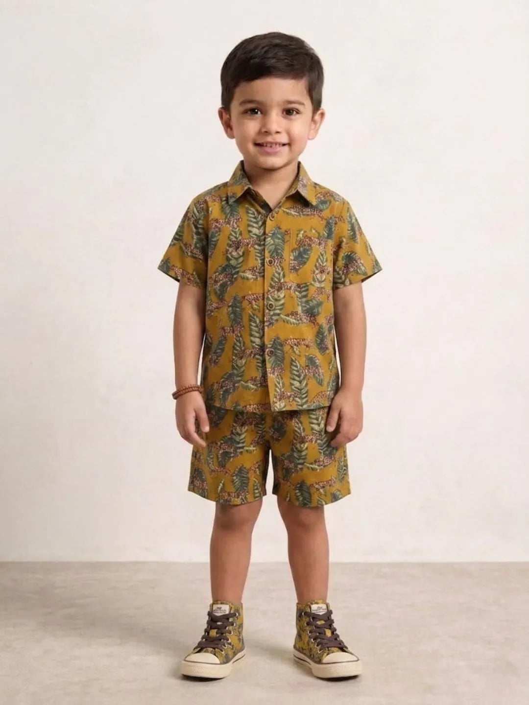 Child wearing a mustard yellow patterned shirt and shorts set on a plain background