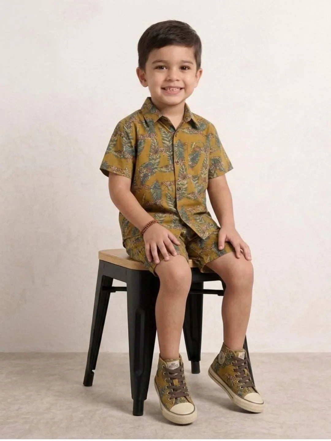 Child wearing a patterned outfit sitting on a black stool against a plain background
