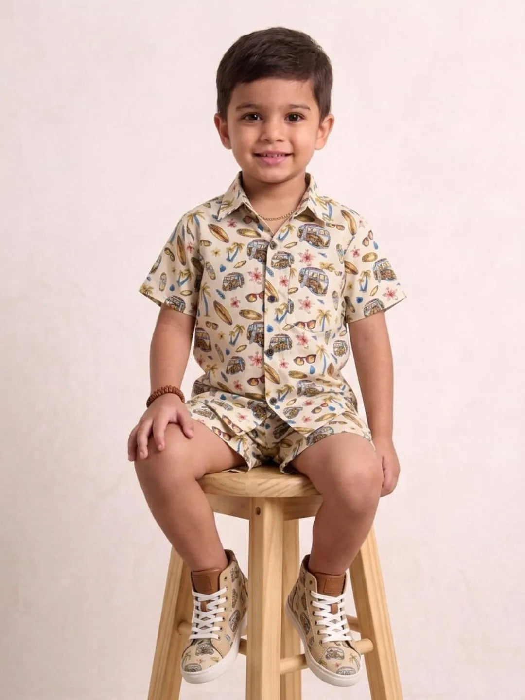 Child sitting on a stool wearing a patterned shirt and shorts set against a plain background