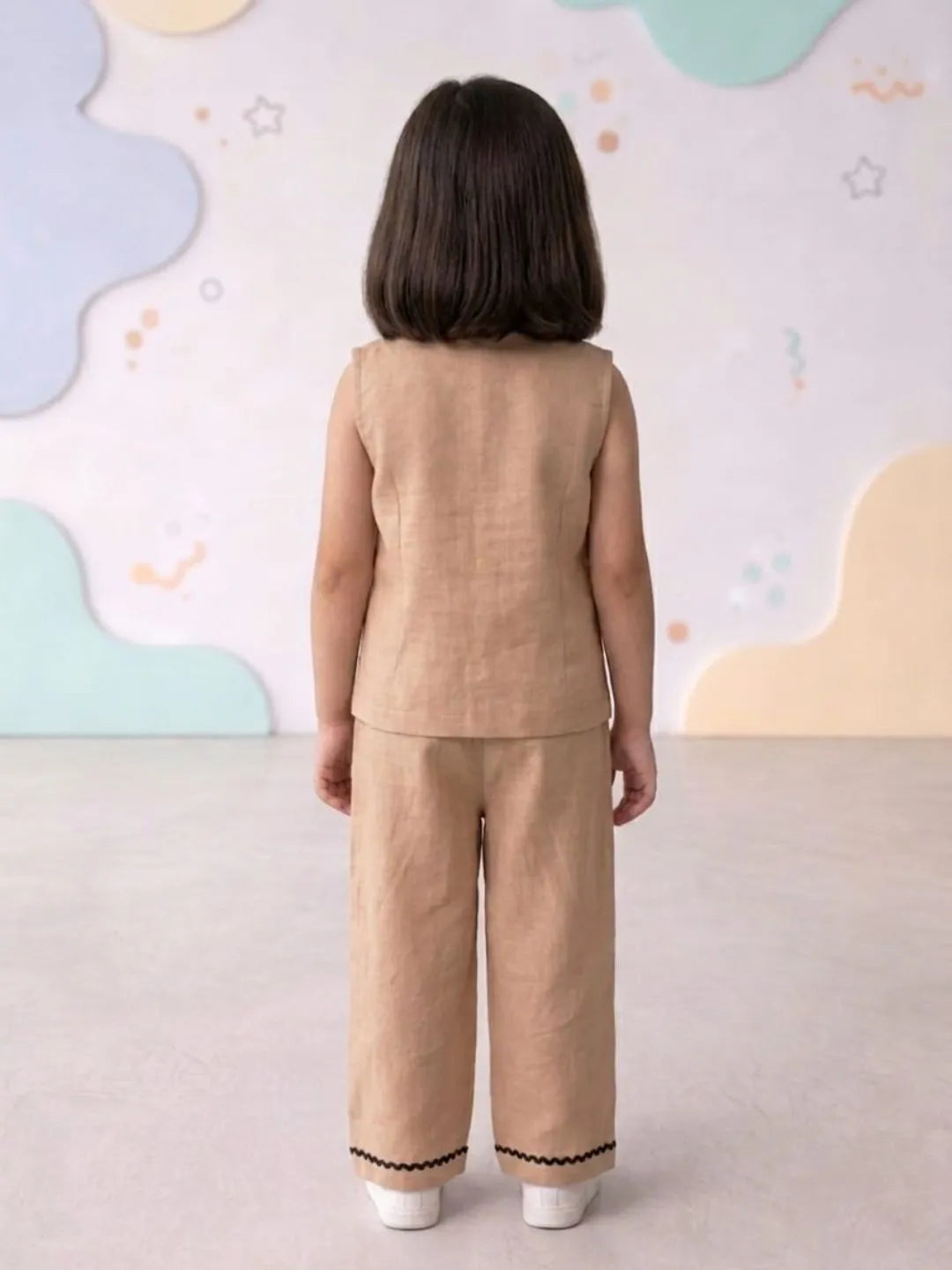 Child wearing a beige outfit with a patterned wall in the background