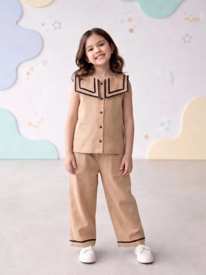 Young girl wearing a beige outfit with black trim against a colorful wall.