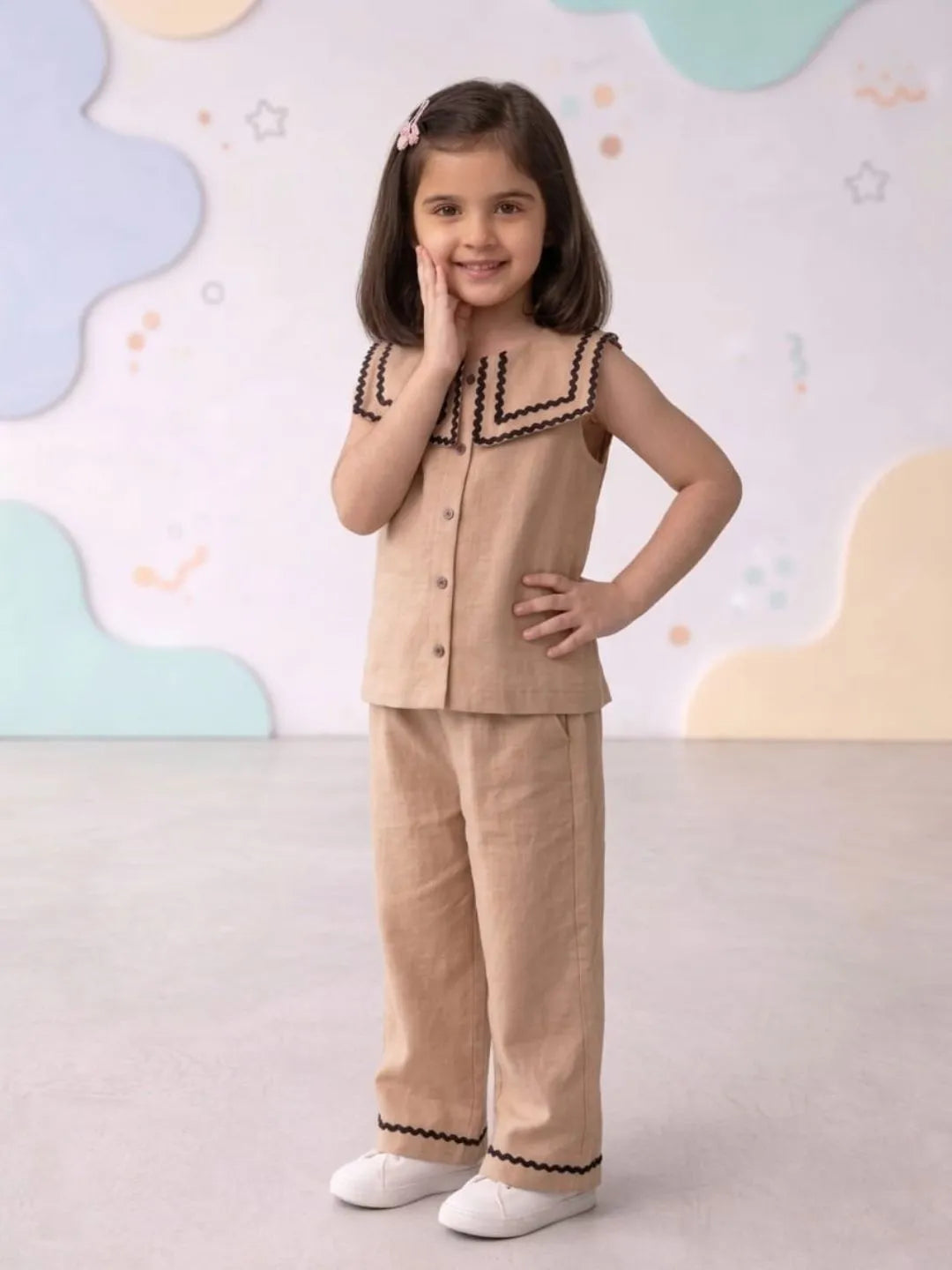 Young girl wearing a beige outfit with black trim against a colorful abstract background