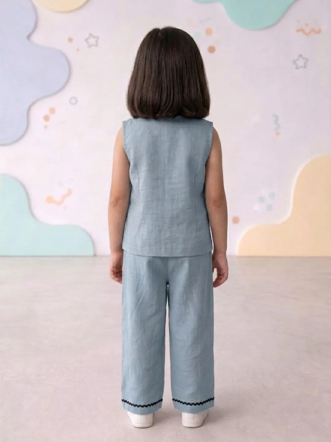 Child wearing a light blue sleeveless top and pants set against a colorful wall.