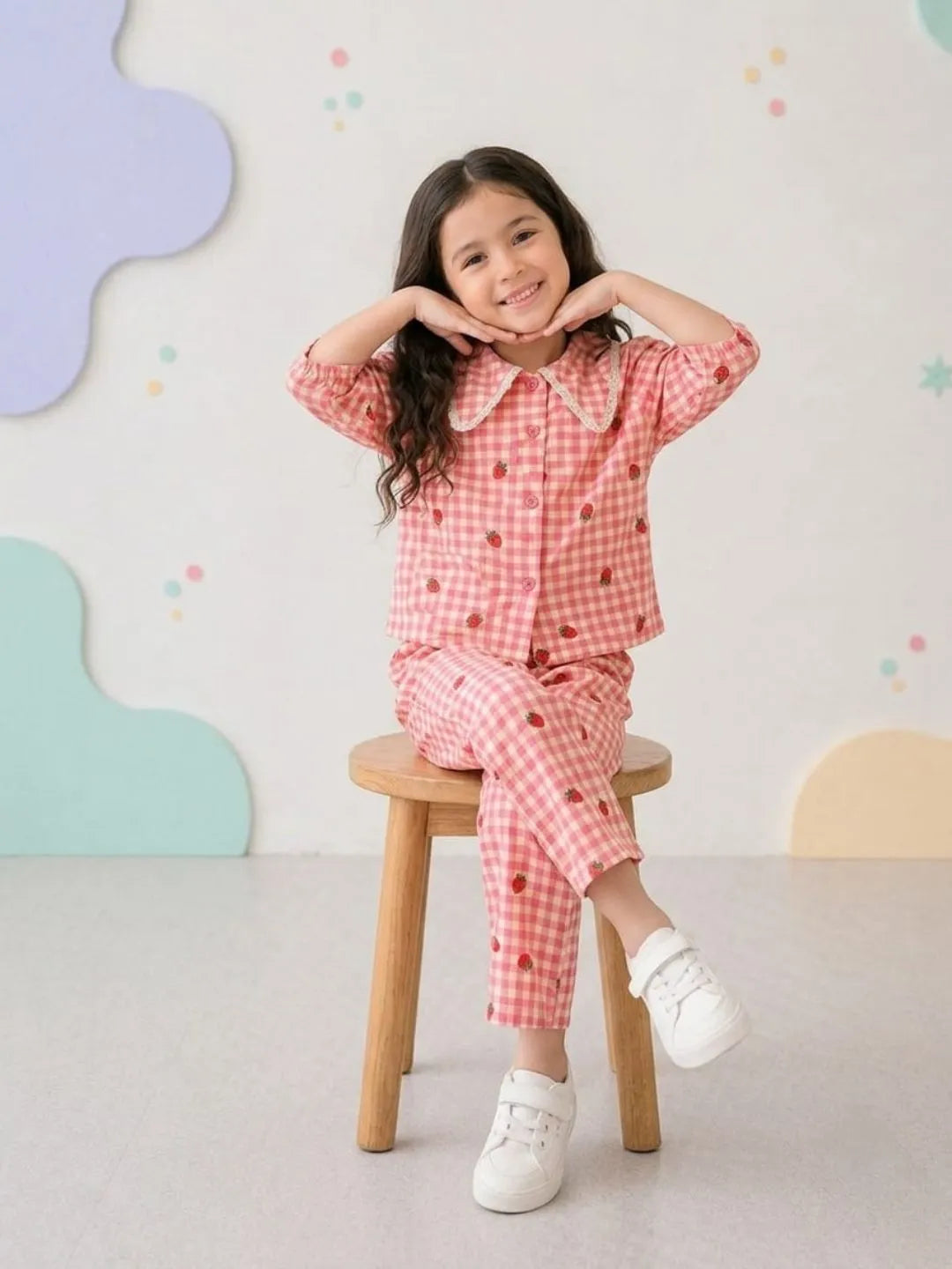 Child wearing a pink checkered outfit sitting on a wooden stool with a colorful wall in the background