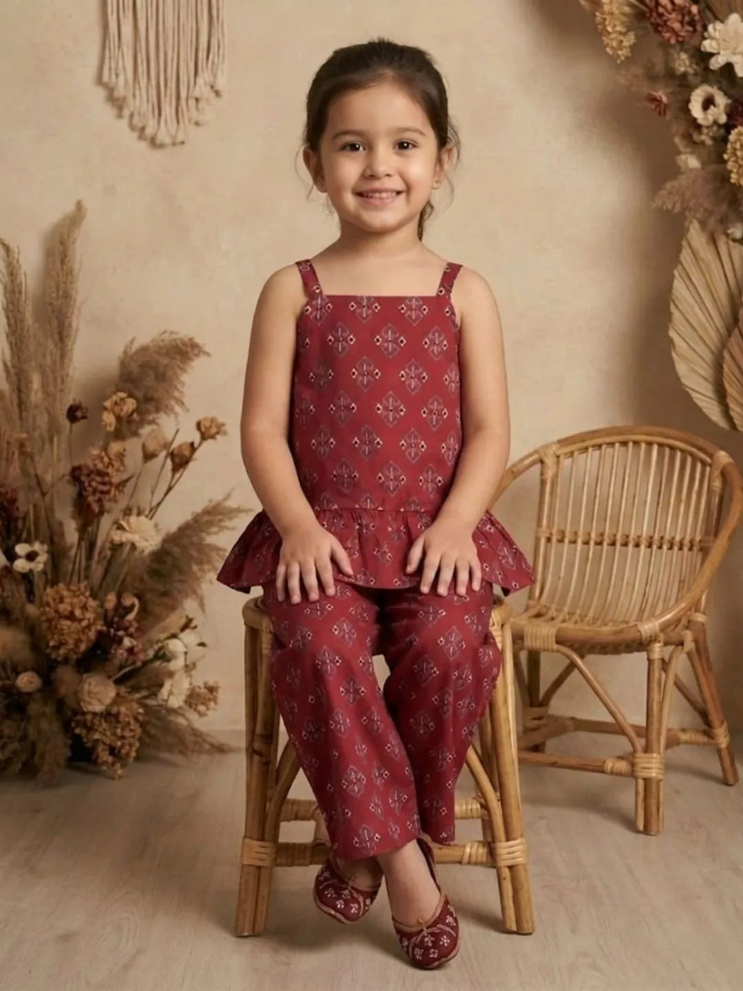 Girl sitting wearing red printed co-ord set with peplum top and wide leg pants