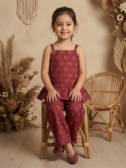 Girl sitting wearing red printed co-ord set with peplum top and wide leg pants